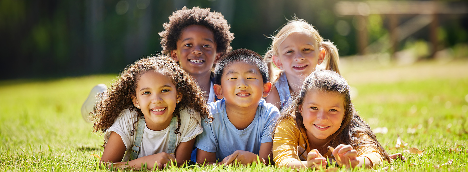 A group of five children posing for a photo outdoors on a sunny day.