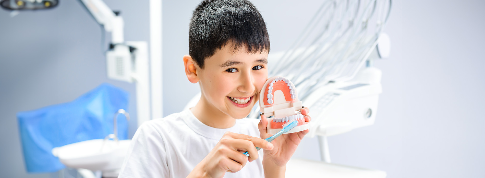 A young boy with a bright smile holds a model of a human eye, surrounded by medical equipment and dental tools, suggesting an educational or interactive learning environment.