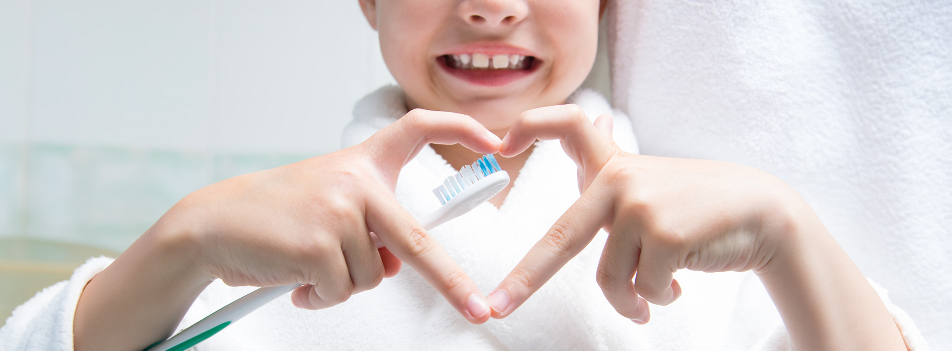 The image shows a person making a heart shape with their hands against a background that includes a towel and a toothbrush, suggesting a bathroom setting.
