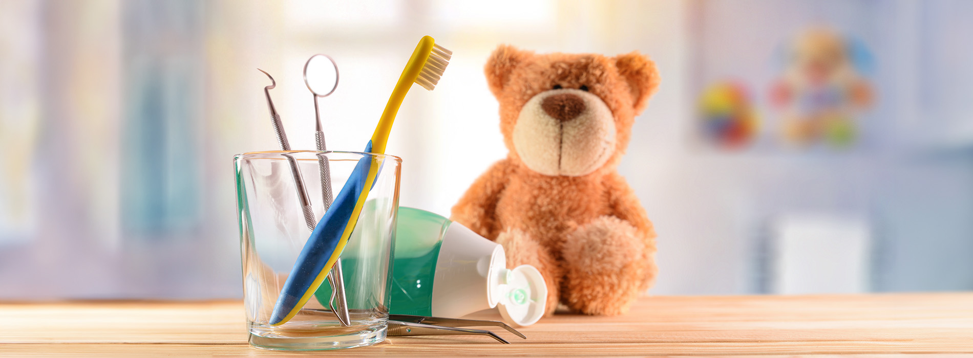 A teddy bear sitting next to a cup of toothbrushes on a table.