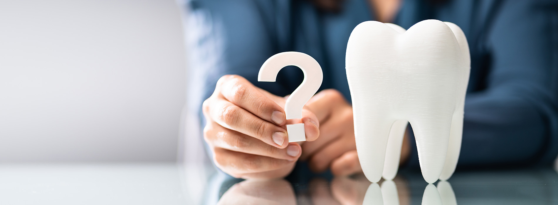 The image shows a person s hand holding a toothbrush with the number two on it, placed next to a pair of white teeth models, against a blurred background that suggests an indoor setting.
