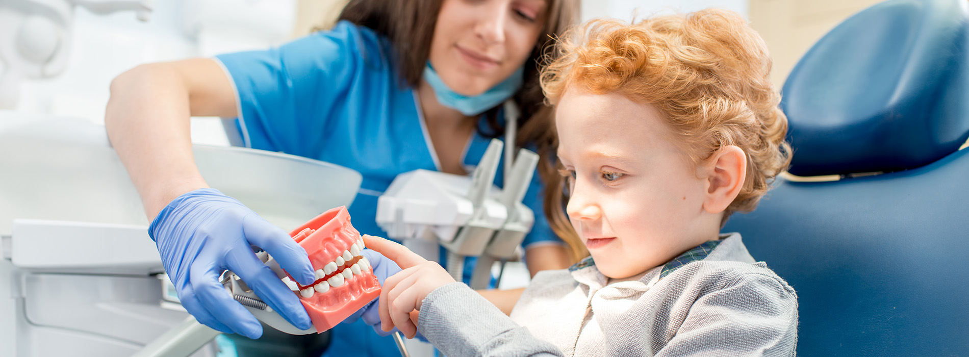 A young child being assisted by a dental hygienist with a cup of water during a dental checkup.