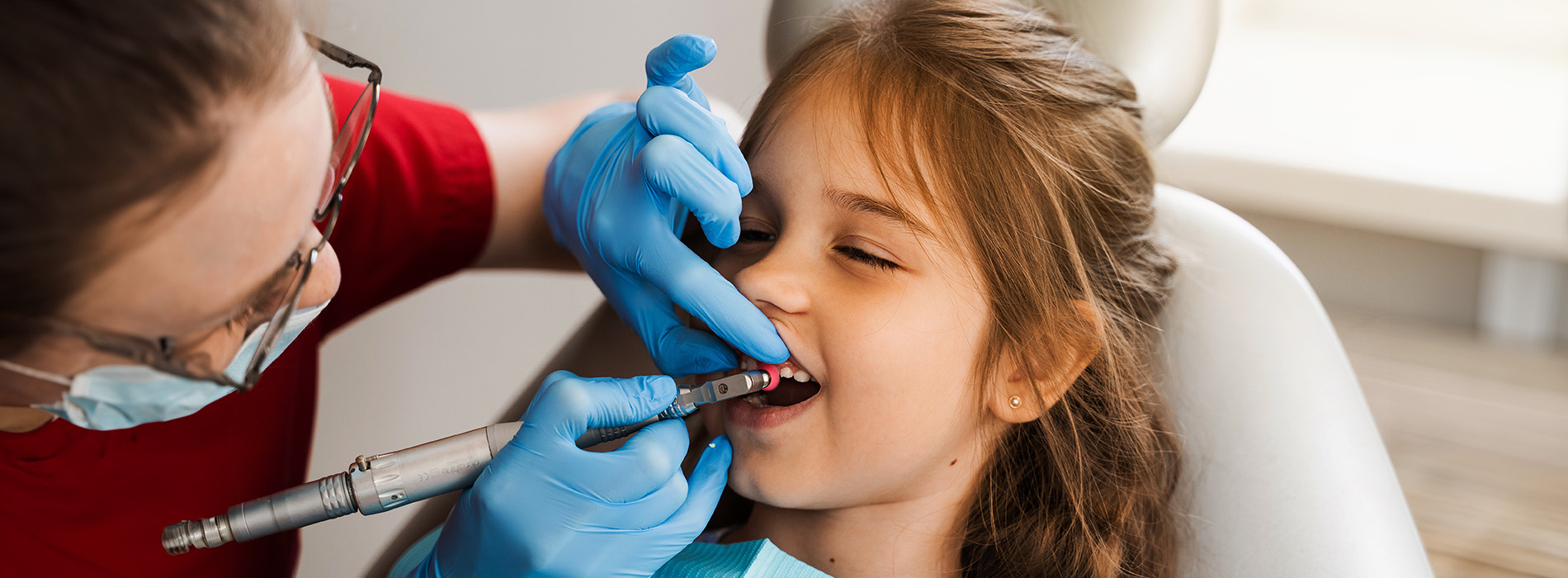 A dental hygienist performing a cavity filling on a young child s tooth while a woman watches.