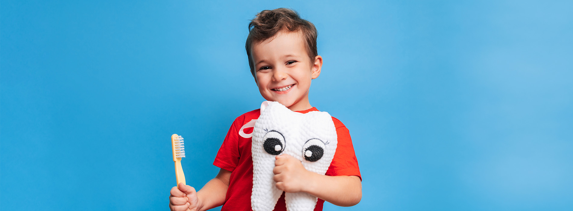 A young child holding a stuffed animal in front of a blue background.