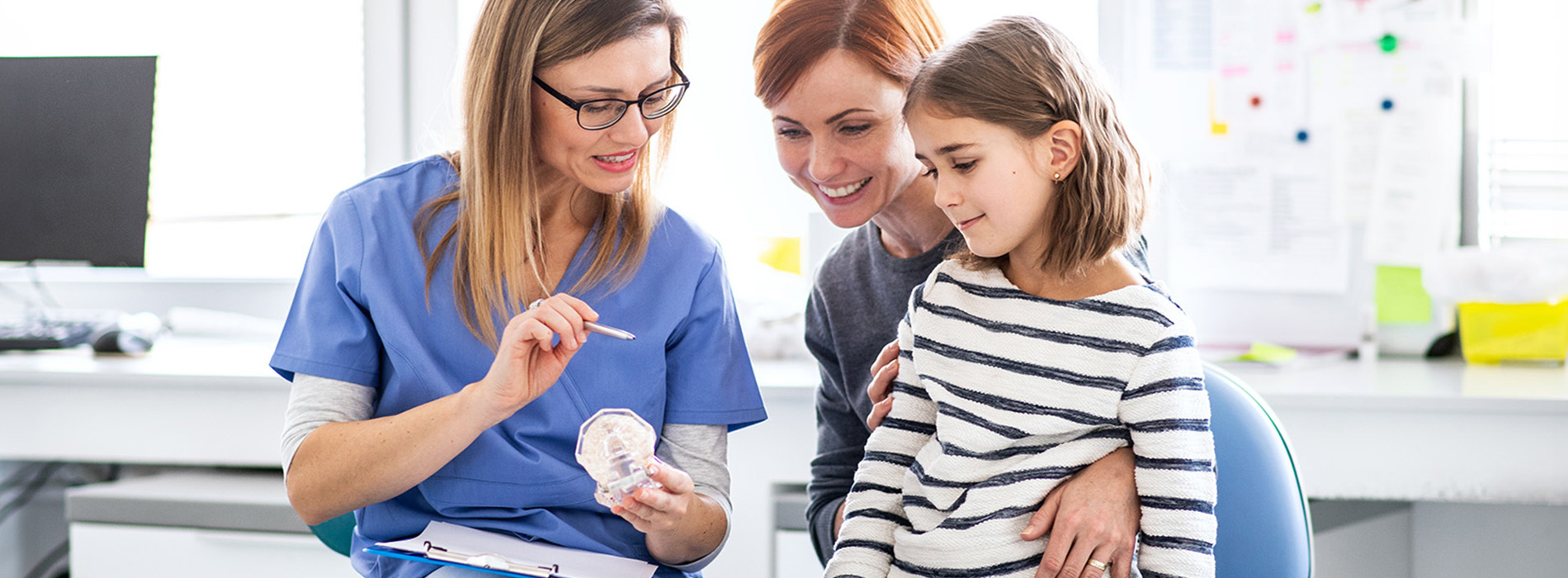 A group of people, including a woman in a white coat who appears to be a nurse, gathered around a computer screen, engaged in an activity with a young child.