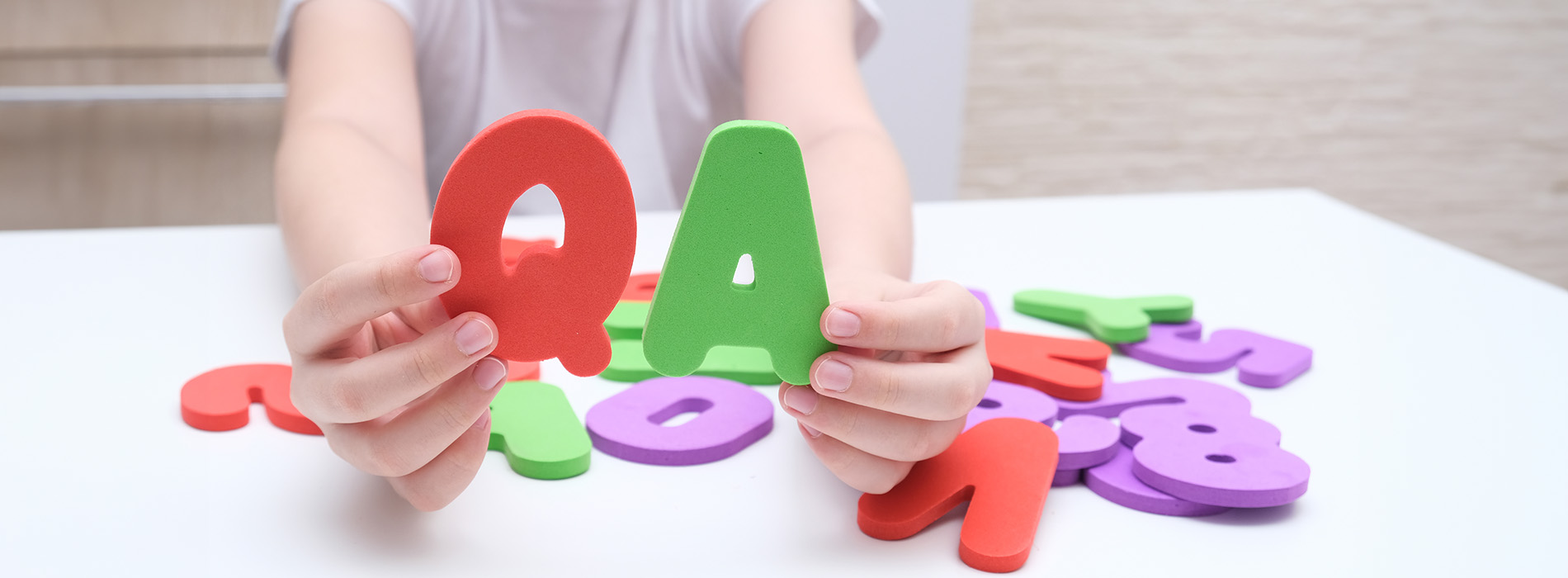 A child s hands holding colorful letter magnets on a white surface.