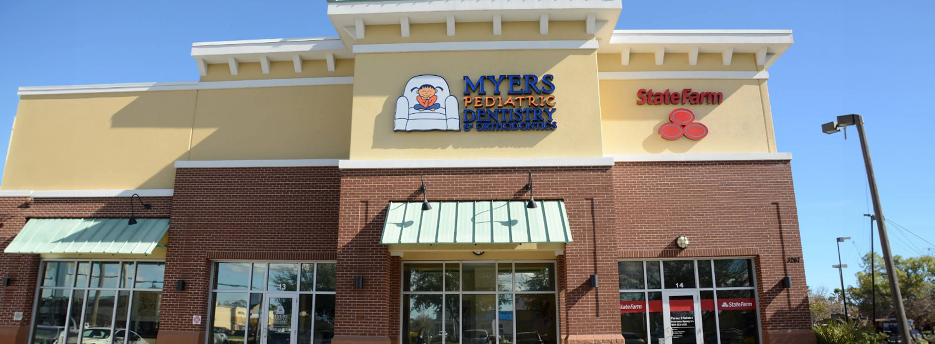 This is a color photograph of an outdoor shopping plaza with a storefront featuring a sign that reads Myzee Sports and other businesses, under a clear sky.