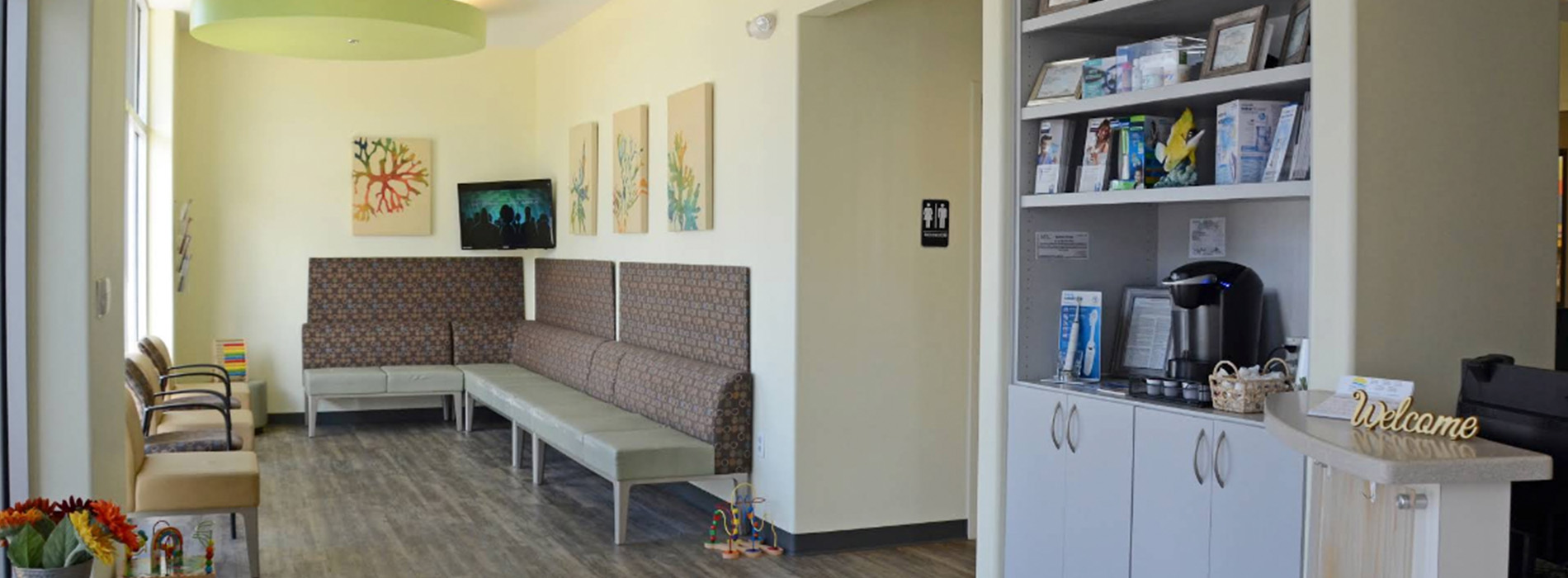 The image shows a well-lit interior space with various furniture pieces including a couch, chairs, tables, and shelves, along with decorative elements like framed pictures on the walls and a potted plant.