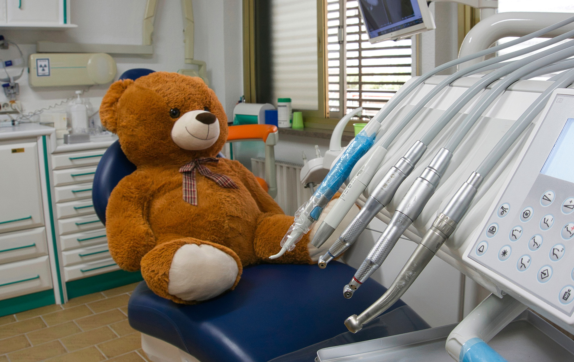 A teddy bear sits in a dentist s chair with dental equipment around, suggesting an unusual scenario for a stuffed toy.