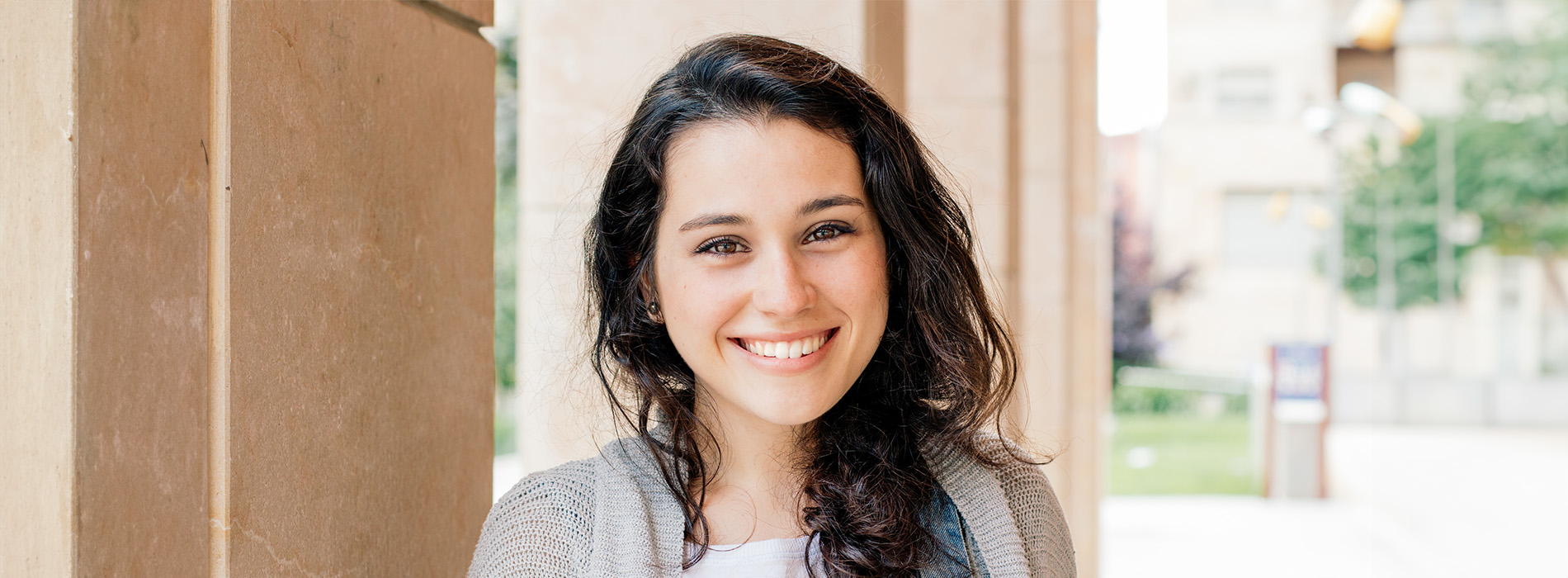 A young woman with dark hair smiling at the camera, posing against an outdoor background with latticework.