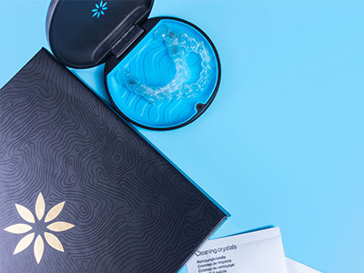The image displays a close-up view of two open cosmetic product boxes with visible branding on a light blue background, one featuring an eye cream and the other a face mask, accompanied by a blue mask in its packaging.