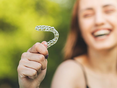 A person is holding up a clear plastic smiley face with their left hand against a blurred background.