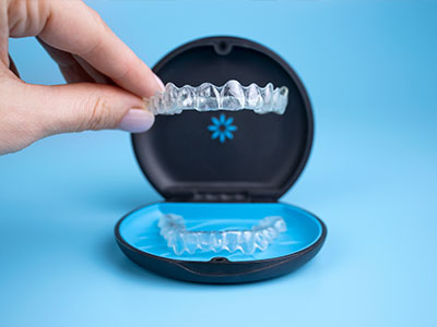 The image shows a person s hand holding an open box containing a clear plastic tray with a set of transparent dental aligners, showcasing the product for display or demonstration purposes.