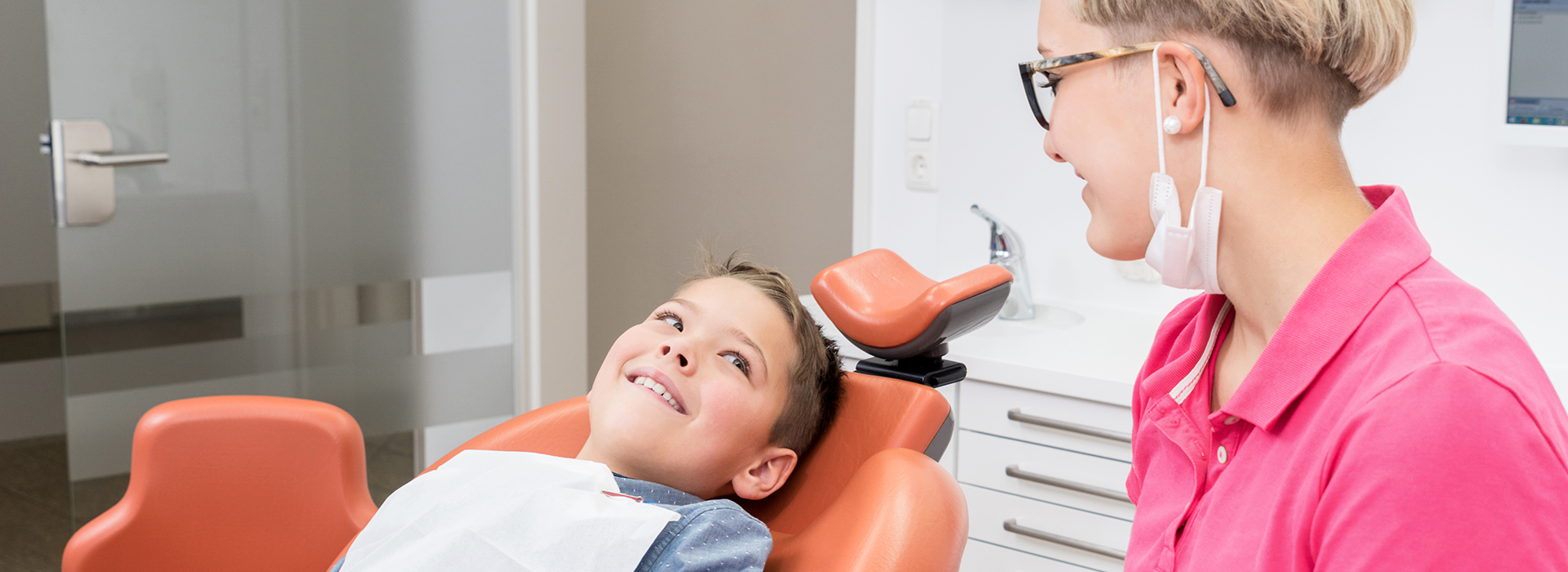 The image shows a dental office setting with a dentist and a patient sitting in chairs, and a smiling woman standing behind them.