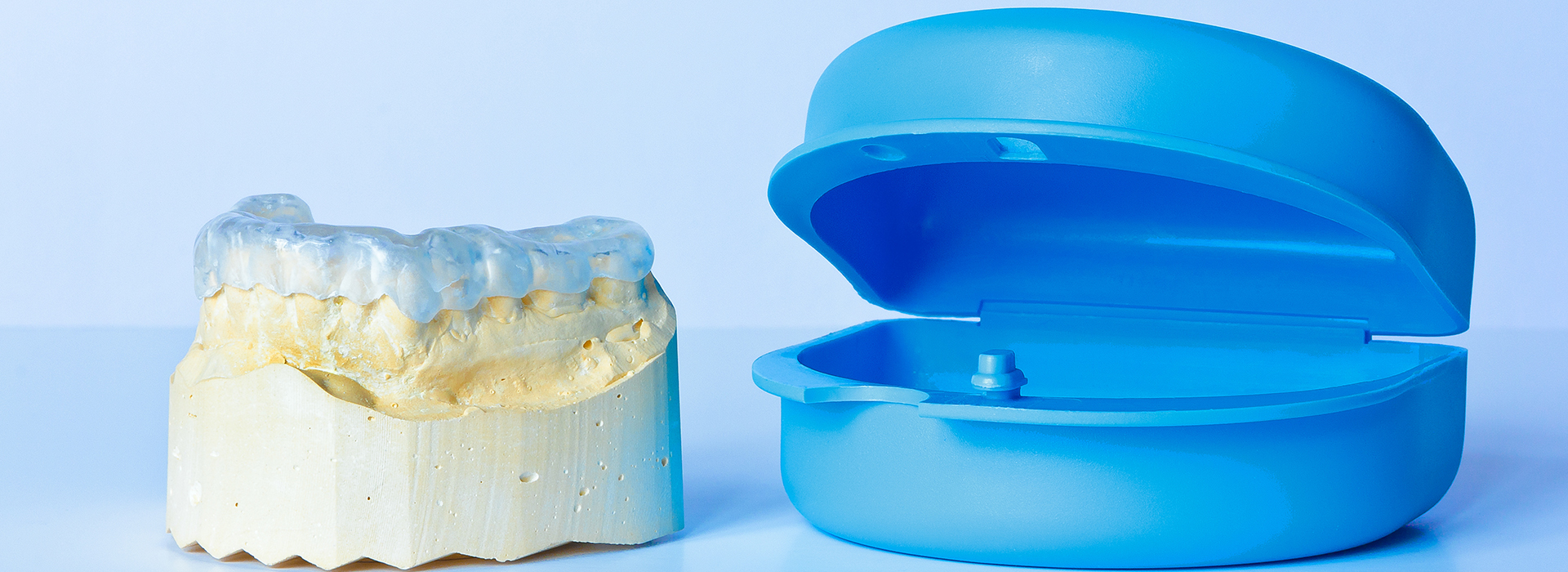 The image shows a blue dental implant fixture next to a yellow plastic toothbrush head.