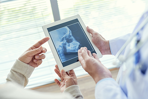 A tablet displaying a medical X-ray is being held by two people, with a doctor looking at it.